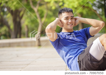 young man training and doing sit ups in park young man training and doing sit ups in park 70907050