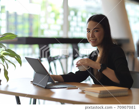Businesswoman working with digital tablet and holding coffee cup 70907081