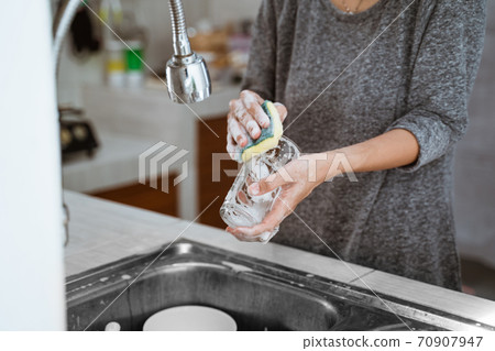 washes dishes with a sponge in the sink 70907947