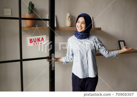 you are welcome. cheerful mature woman in welcome sign and smiling while standing against front door 70908307
