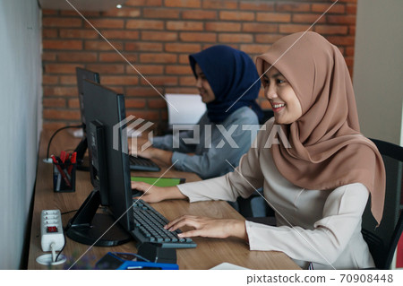muslim business woman working on computer at her desk modern office with her partner muslim business woman working on computer at her desk modern office with her partner 70908448