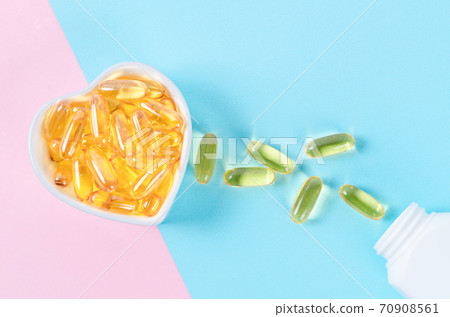 Fish oil capsules in white cup with bottle. 70908561