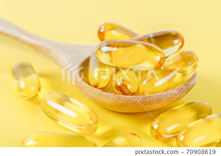Fish oil capsules in wooden spoon. 70908619