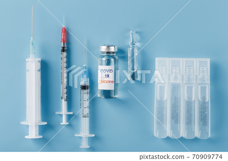 A set of ampoules with the inscription Covid-19 vaccine and a set of syringes against a blue background. A set of ampoules with the inscription Covid-19 vaccine and a set of syringes against a blue background. 70909774