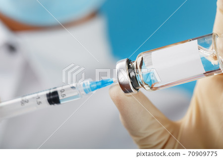 A doctor in rubber gloves holds an ampoule with a vaccine and a syringe, close-up. A doctor in rubber gloves holds an ampoule with a vaccine and a syringe, close-up. 70909775