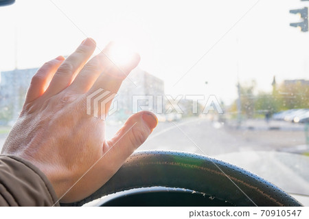 driver's hand at the wheel of the car covers the blinding sun 70910547