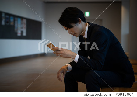 A businessman who is worried about holding a smartphone 70913004