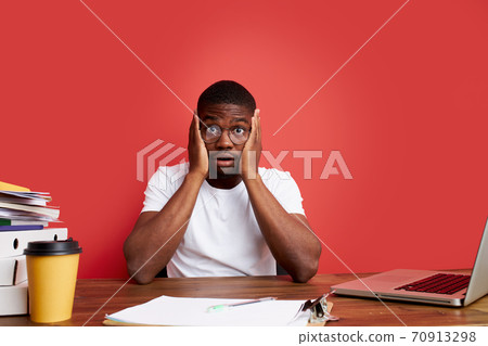 overworked unhappy and frustrated young african man in stress sitting at office desk 70913298
