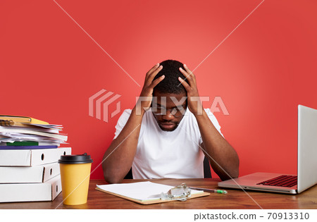 overworked unhappy and frustrated young african man in stress sitting at office desk 70913310