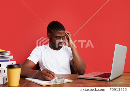 overworked unhappy and frustrated young african man in stress sitting at office desk 70913313