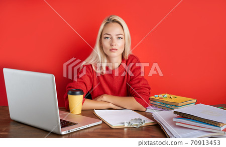 portrait of confident caucasian blonde female sitting at office desk with laptop and papers 70913453