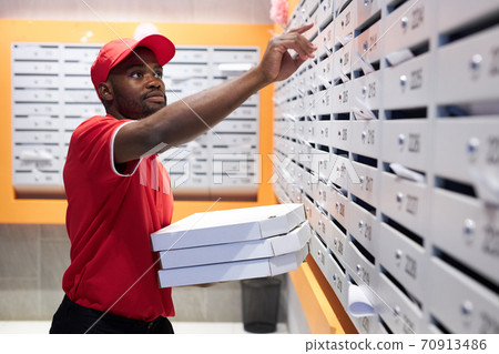 handsome black deliveryman puts order in the mailbox 70913486