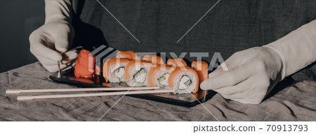 Hands in rubber gloves serve sushi on a black stand. Sushi menu. Hands in rubber gloves serve sushi on a black stand. Sushi menu. 70913793