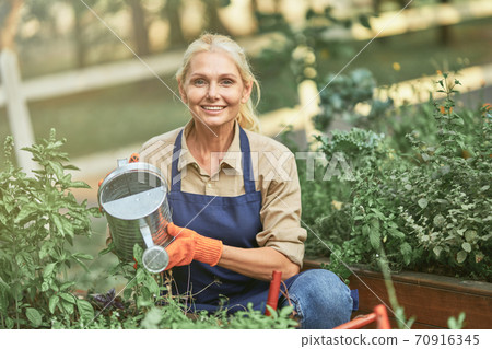 Middle aged caucasian business woman watering plants Middle aged caucasian business woman watering plants 70916345