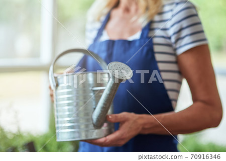 Woman holding watering can in hands standing in greenhouse Woman holding watering can in hands standing in greenhouse 70916346