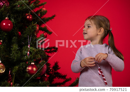 Smiling happy child girl decorating Christmas tree on red studio Xmas background Smiling happy child girl decorating Christmas tree on red studio Xmas background 70917521
