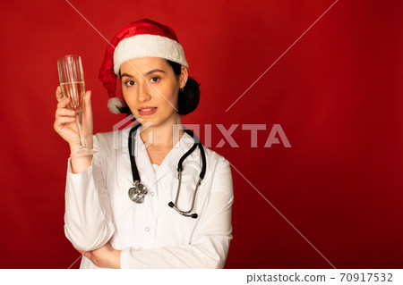 sexy female doctor celebrating Christmas looking at camera with champagne flute sexy female doctor celebrating Christmas looking at camera with champagne flute 70917532