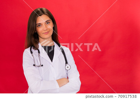 Pretty brunette female doctor posing crossed arms isolated on red studio Pretty brunette female doctor posing crossed arms isolated on red studio 70917538