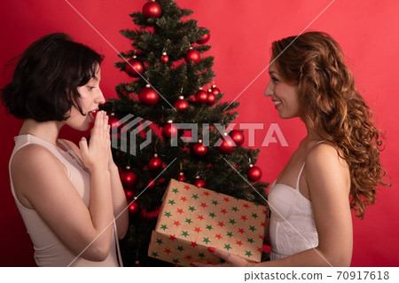 Pretty lesbian woman presents Christmas gift to surprised girlfriend, New Year Pretty lesbian woman presents Christmas gift to surprised girlfriend, New Year 70917618