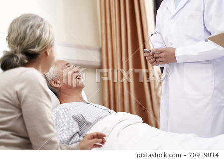 senior asian man male patient lying on bed talking to doctor in hospital ward 70919014