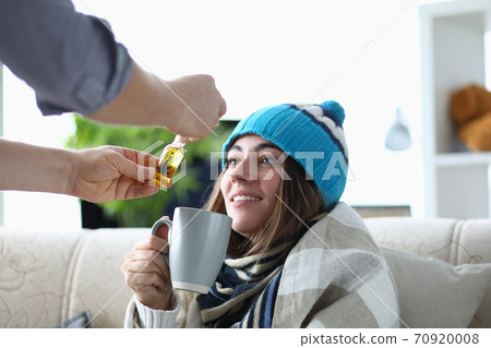 Young woman addict sits in hat and scarf on sofa at home with cup with marijuana extract portrait 70920008