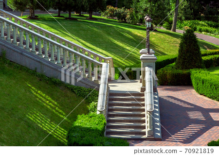A stone staircase with balustrades railing down into the garden with landscaped green lawns and clipped bushes. 70921819