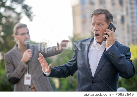 Mature man speaking on the phone, pushing male journalist away Mature man speaking on the phone, pushing male journalist away 70922649