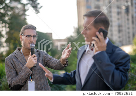Mature man speaking on the phone, unwilling to give interview to male journalist 70922651