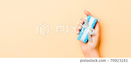 Flat lay of woman hands holding gift wrapped and decorated with bow on gold background with copy space. Christmas and holiday concept Flat lay of woman hands holding gift wrapped and decorated with bow on gold background with copy space. Christmas and holiday concept 70923281