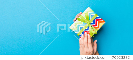 Woman arms holding gift box with colored ribbon on blue table background, top view and copy space for you design Woman arms holding gift box with colored ribbon on blue table background, top view and copy space for you design 70923282