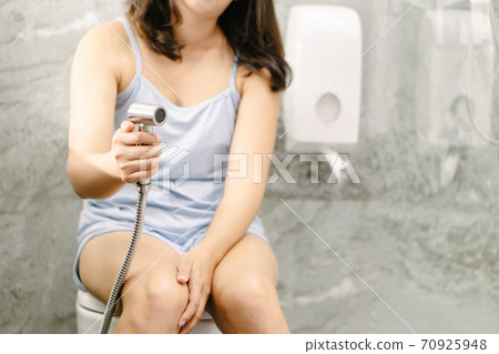 Woman hand using Chromium bidet shower sitting on toilet 70925948