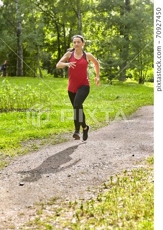 Active mature woman runs in public park. Active mature woman runs in public park. 70927450