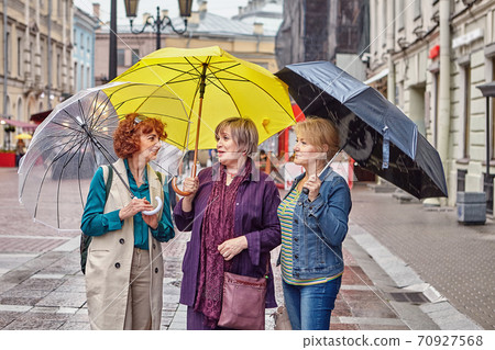 Senior women with umbrellas talk on street. 70927568