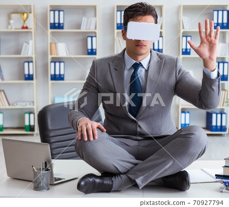 Businessman in virtual reality VR glasses meditating at desk top Businessman in virtual reality VR glasses meditating at desk top 70927794