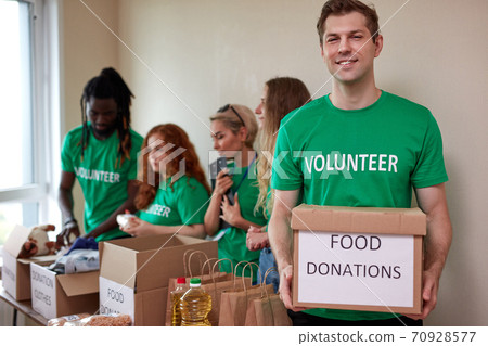 portrait of affable volunteer man in green t-shirt holding donation box in hands portrait of affable volunteer man in green t-shirt holding donation box in hands 70928577