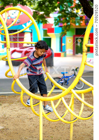 Asian boy is climbing on a playground equipment in a school. Asian boy is climbing on a playground equipment in a school. 70929520