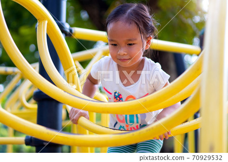 Asian girl is climbing on a playground equipment in a school. 70929532