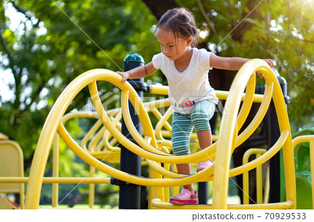 Asian girl is climbing on a playground equipment in a school. Asian girl is climbing on a playground equipment in a school. 70929533