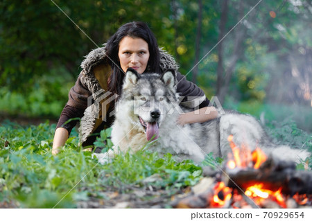 Portrait of a pretty white woman with an Alaskan Malamute dog by the fire Portrait of a pretty white woman with an Alaskan Malamute dog by the fire 70929654