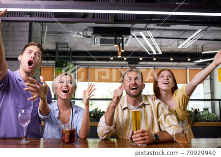 happy friends drinking beer, watching sport game or football match together in bar 70929940