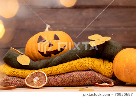 Halloween pumpkin and stack of colorful winter sweaters on wooden. Cozy autumn decoration with lantern Halloween pumpkin and stack of colorful winter sweaters on wooden. Cozy autumn decoration with lantern 70930697
