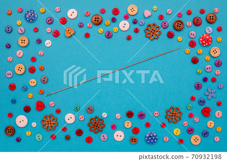 Multi-colored buttons are scattered on the table, a needle. Accessories for sewing. Top view with copy space, flat lay. Multi-colored buttons are scattered on the table, a needle. Accessories for sewing. Top view with copy space, flat lay. 70932198