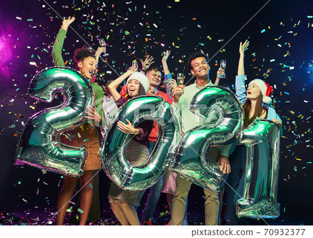 New Year celebration. Group of young happy multiracial friends holding silver foil balloons in form of numbers 2021, dancing and having fun, confetti falling in the air New Year celebration. Group of young happy multiracial friends holding silver foil balloons in form of numbers 2021, dancing and having fun, confetti falling in the air 70932377