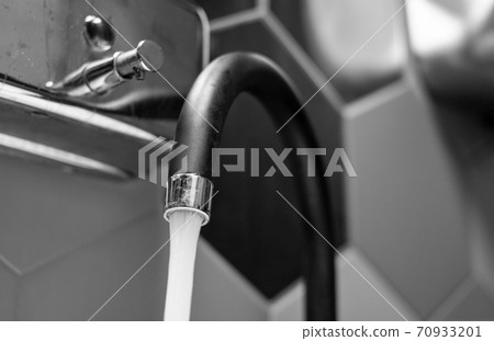 Tap water flows against a background of black and white tiles.selective focus. Tap water flows against a background of black and white tiles.selective focus. 70933201