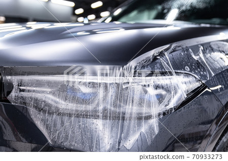 Car detailing specialist installing protective transparent foil 70933273
