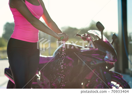 Close up woman's hands squeeze moisture out of the rag while wipes sport motorcycle at self service car wash. Close up woman's hands squeeze moisture out of the rag while wipes sport motorcycle at self service car wash. 70933404