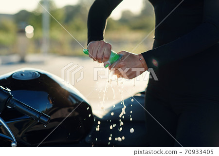Close up woman's hands squeeze moisture out of the rag while wipes sport motorcycle at self service car wash. 70933405