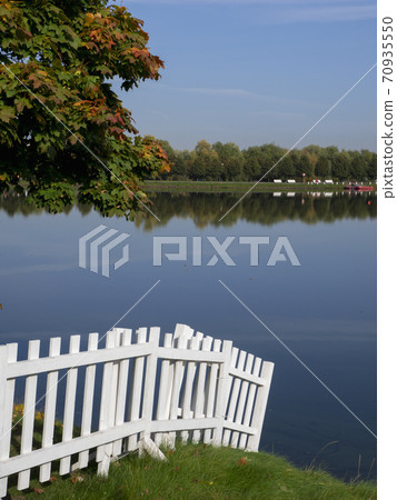 White wooden fence with green lawn and water. 70935550
