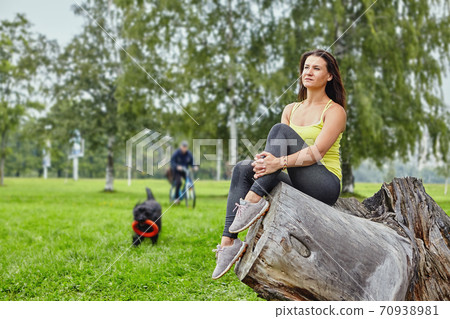 Pensive young lady sits in park during dog walking. Pensive young lady sits in park during dog walking. 70938981