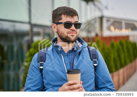 Young man drinks coffee from paper cup outside. 70938993